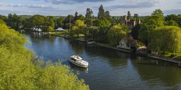 Aerial of Le Boat Horizon 4 houseboat passing Oakley Court Hotel along River Thames, Water Oakley, near Windsor, Berkshire, England, United Kingdom